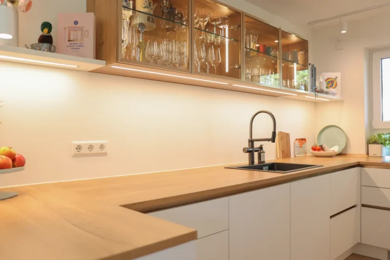 Elegante Spüle mit dunkler Armatur und Blanco CHOICE System in einer U-Küche mit warmem Holzkontrast und zurückhaltendem LED-Lichtkonzept.