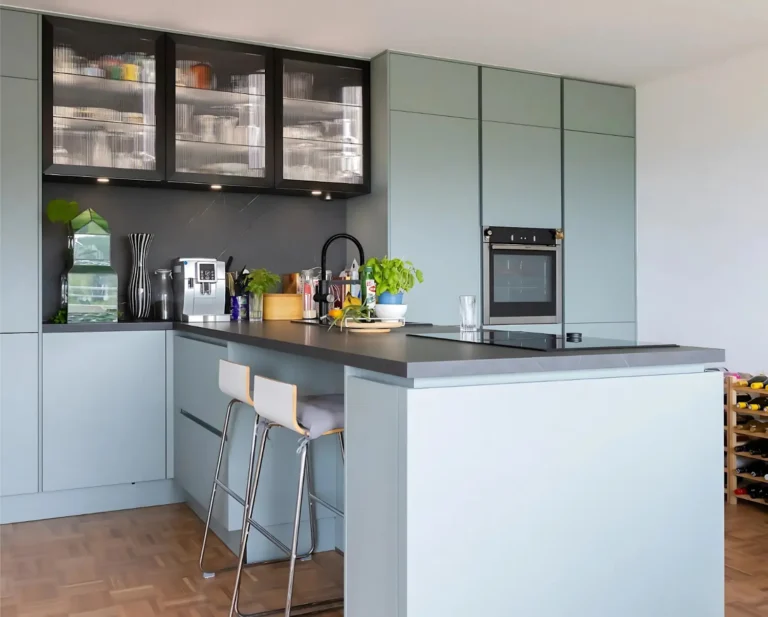 T-förmige Küche mit Barhockern an der Kochinsel, durchgängiges Design mit sanftgrünen Fronten und dunkler Arbeitsfläche