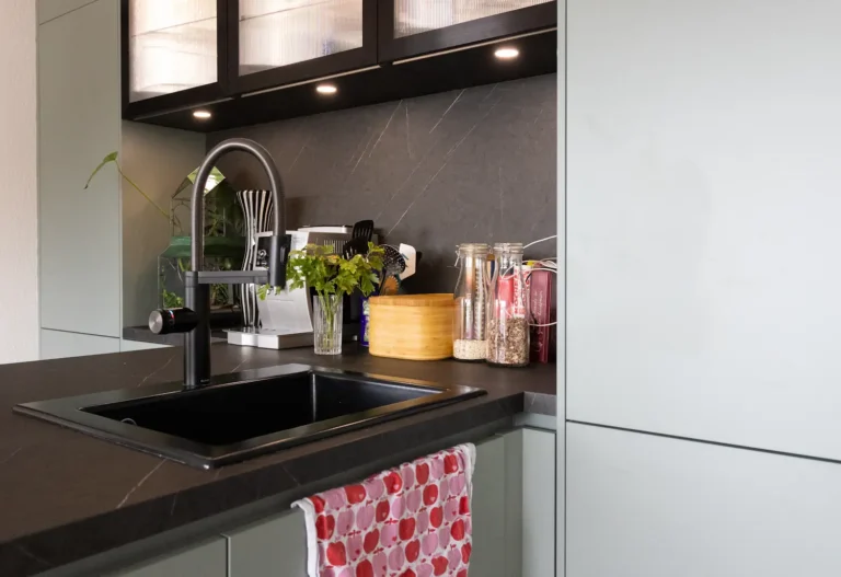 Schwarze Einbauspüle mit Armatur, Vorratsgläsern, frischen Kräutern und Küchenutensilien auf der Arbeitsfläche