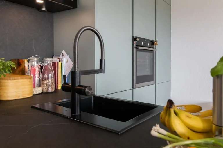 Moderne Küche mit schwarzer Einbauspüle und Armatur, im Hintergrund griffloser Hochschrank in Mintgrün mit integriertem Backofen